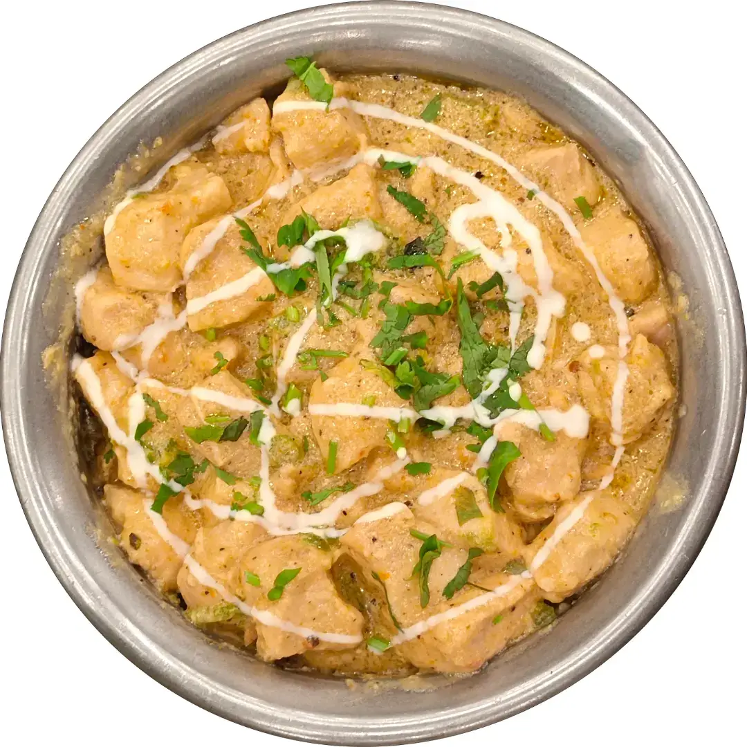 A metal serving bowl of creamy chicken white karahi, garnished with fresh cilantro and a drizzle of cream.